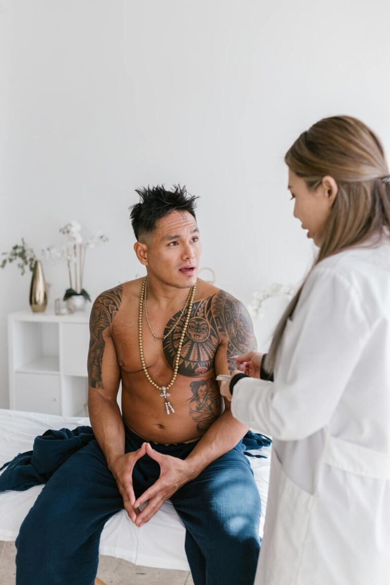 A shirtless man with tattoos discusses health with a female doctor indoors.